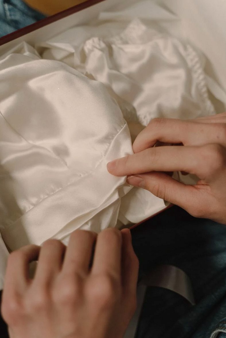 Woman's hands exploring silky white lingerie from a gift box, showcasing delicate satin texture.